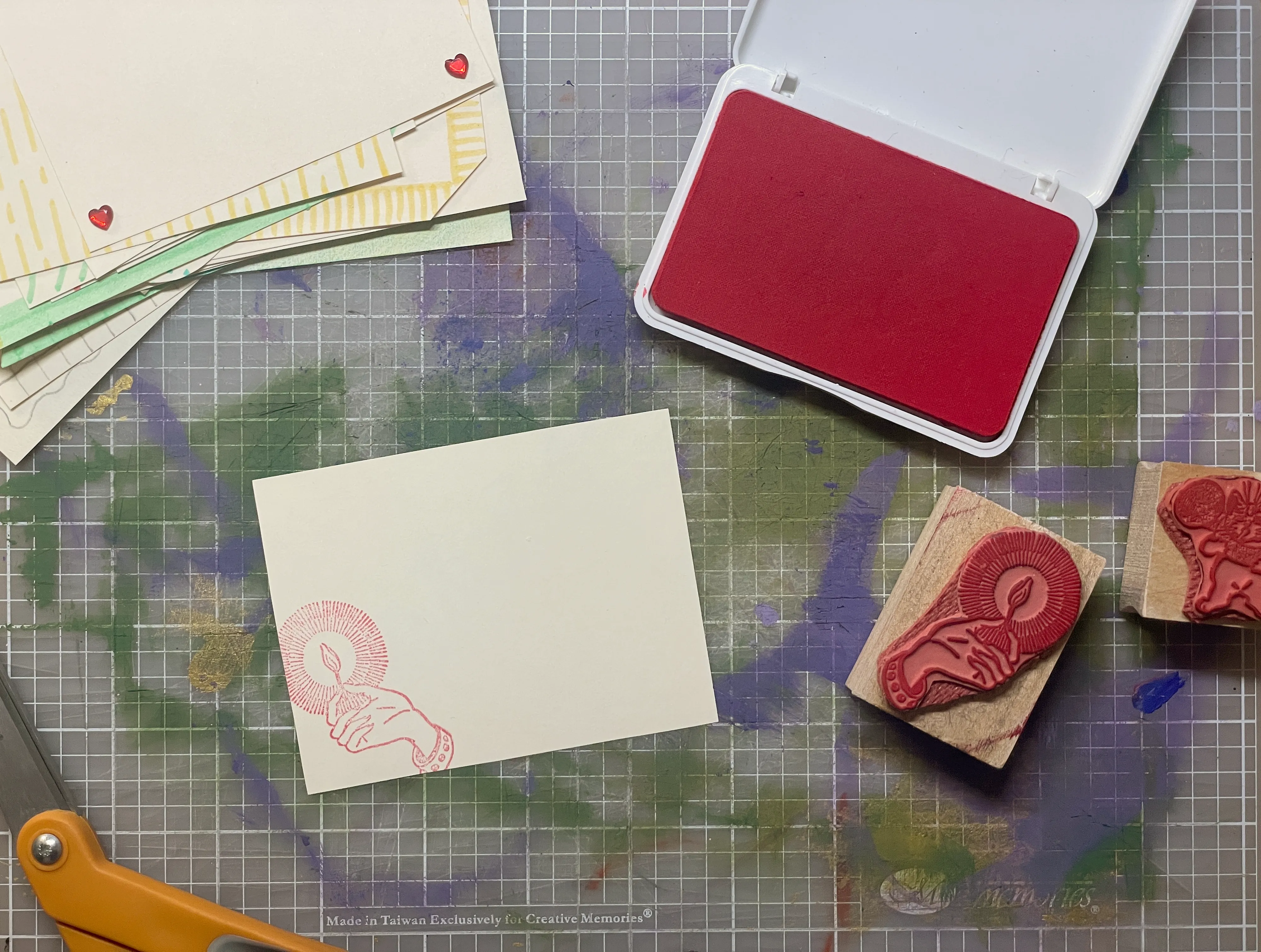 Two stamps sit beside small rectangular piece of cream-color card stock. There is a red stamp on the paper with a hand holding a match alight.